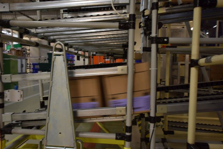 Az AGV a gyártósornál kialakított görgőpolcos tárolók teljes tartalmát, tehát az adott gyártóhely kartondobozokban összekészített összes készáruját felveszi